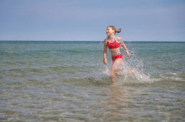 Beautiful child girl playful running in water at sea in summer