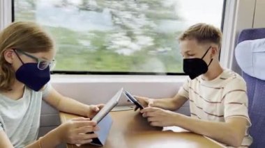 60fps 4K video of two happy children in medical masks traveling on train and playing with tablets