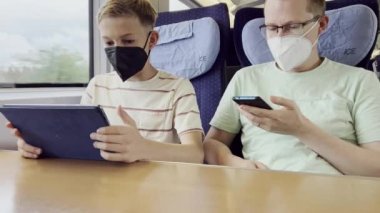 Father with his teen son traveling with train and using cellphone and tablet during vocation