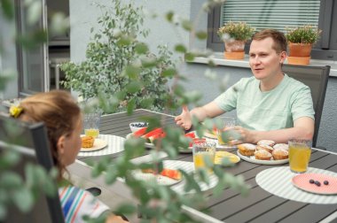 Teen son and dad having breakfast outdors in backyard