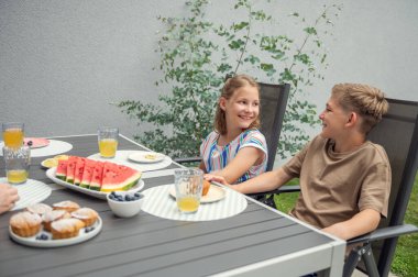 Teen brother and suster having breakfast outdoors in the backyard