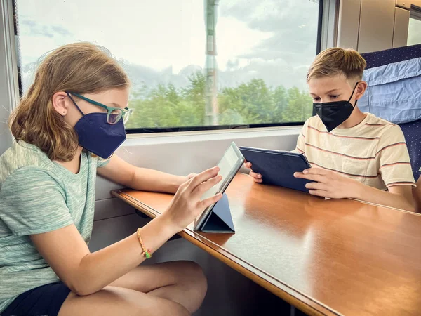 Teen brother and sister travelling on railway and play with tablets in the train