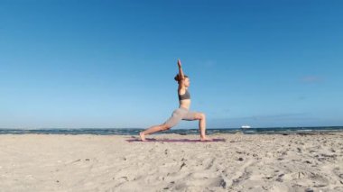 4k 60fps morning yoga routine at Baltic sea coastline over clear blue sky with large vessel in background