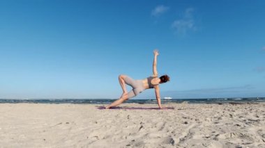 4k 60fps morning yoga routine at Baltic sea coastline over clear blue sky with large vessel in background
