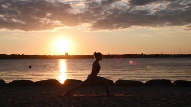 Gün batımında Baltık deniz kıyısında yoga yapan bir kadının yavaş çekim videosu.