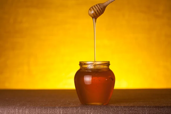 Honey jar with dipper and flowing honey — Stock Photo, Image