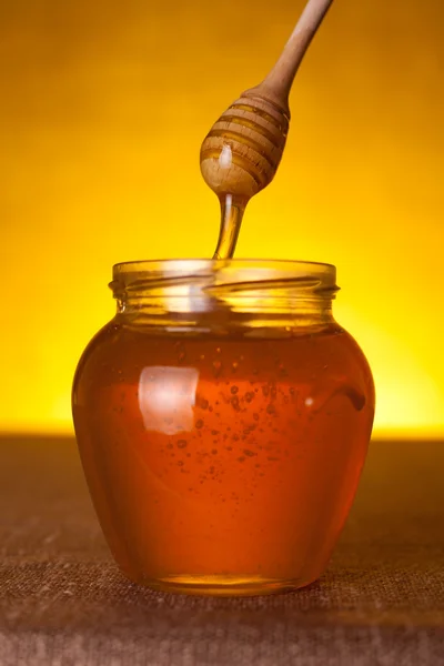 Frasco de mel com dipper e mel fluindo — Fotografia de Stock