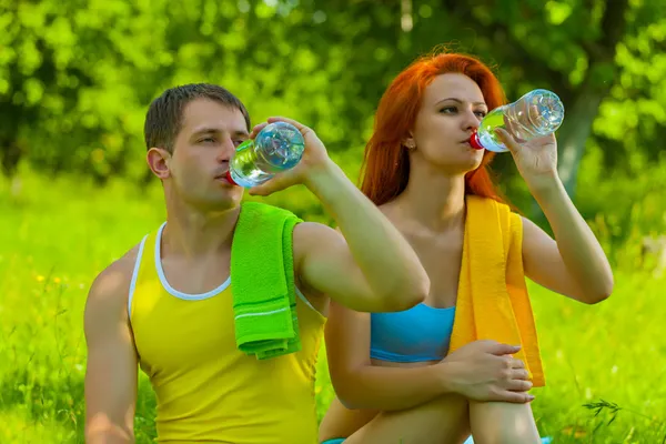 Un uomo e una donna che bevono acqua dalle bottiglie — Foto Stock