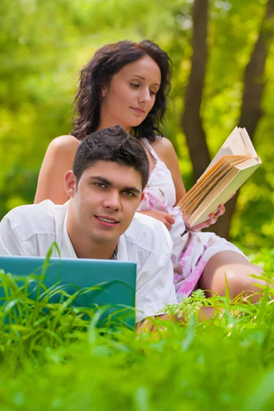 Молодая пара лежит с ноутбуком и книга в парке — стоковое фото