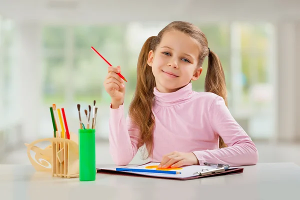 Une jeune fille avec un crayon assis à table — Photo