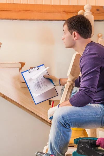 Ein junger Tischler mit einem Bauplan und auf einer Leiter sitzend — Stockfoto