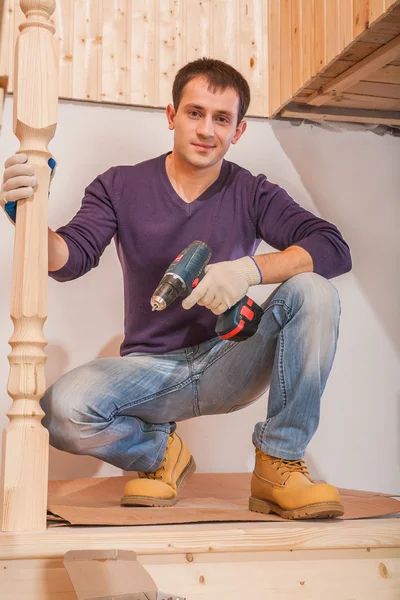 Ein junger Tischler sitzt und hält Akkubohrmaschine in der Hand — Stockfoto