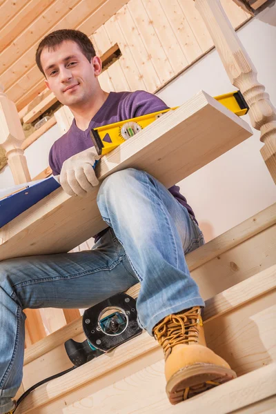 A young worker siiting on step of ladder and holding wooen board — Stock Photo, Image