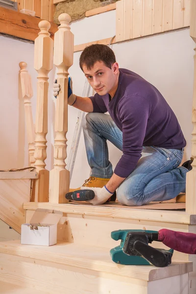 Молодой рабочий фиксирует деревянную лестницу — стоковое фото
