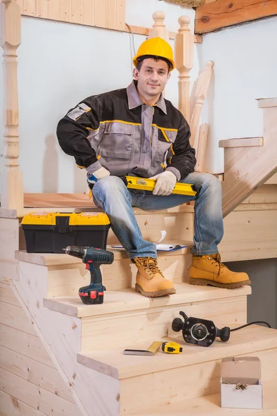 Contractor sitting on steps of wooden ladder with tools — Stock Photo, Image