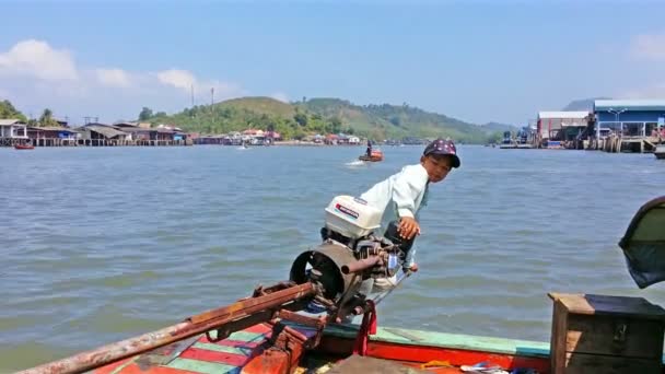 Ranong, thailand - 11 februari 2014: niet-geïdentificeerde lokale kleine jongen beheren met motor op houten lange boot — Stockvideo