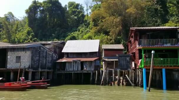 Ranong, thailand - 11 februari 2014: huizen op palen langs de oever met afgemeerd houten boten — Stockvideo