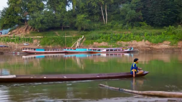 LUANG PRABANG, LAOS - 08 DEC 2013: Unidentified man row by traditional wooden boat on calm river near wooden bridge — Stock Video