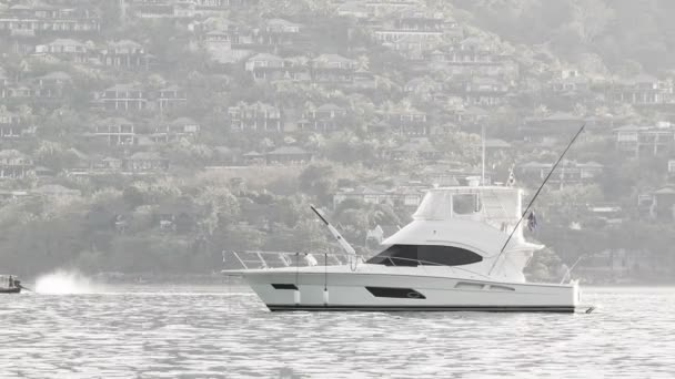 PHUKET, TAILANDIA - 05 OCT 2013: Yate de motor blanco anclado en un mar tranquilo y limpio con edificios modernos en el fondo — Vídeo de stock