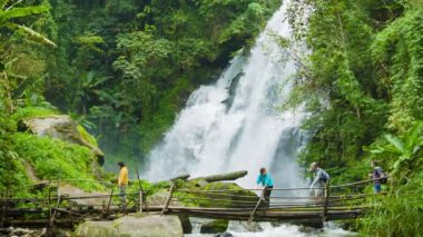 Chiang mai, Tayland - yaklaşık Aralık 2013: turist çapraz nehir bir kaygan bambu Köprüsü'nde arka planda bir şelale