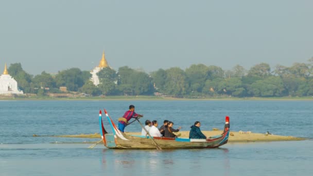 MANDALAY, MYANMAR - 13 ENE 2014: Barco de madera con la gente se mueven en el lago Taungthaman con templos budistas en el fondo — Vídeos de Stock