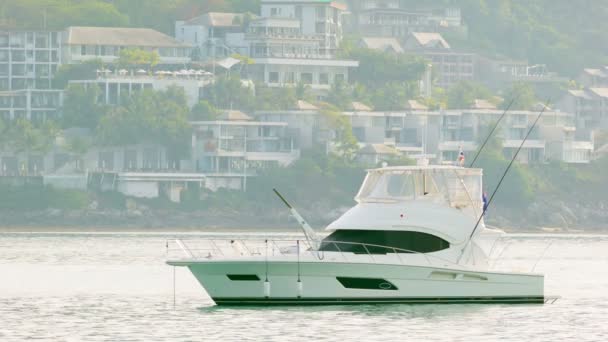 PHUKET, THAILAND - 05 OCT 2013: White motor yacht anchored in calm clean sea with modern buildings on background — Stock Video