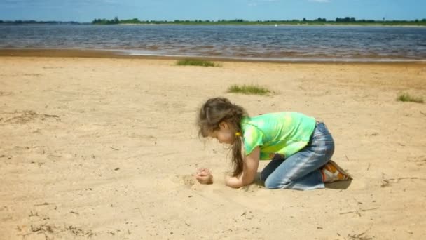 Vídeo 1080p - Menina brincando com areia na margem de um grande rio — Vídeo de Stock