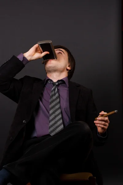 Молодой бизнесмен курит сигарету и пьет бренди — стоковое фото