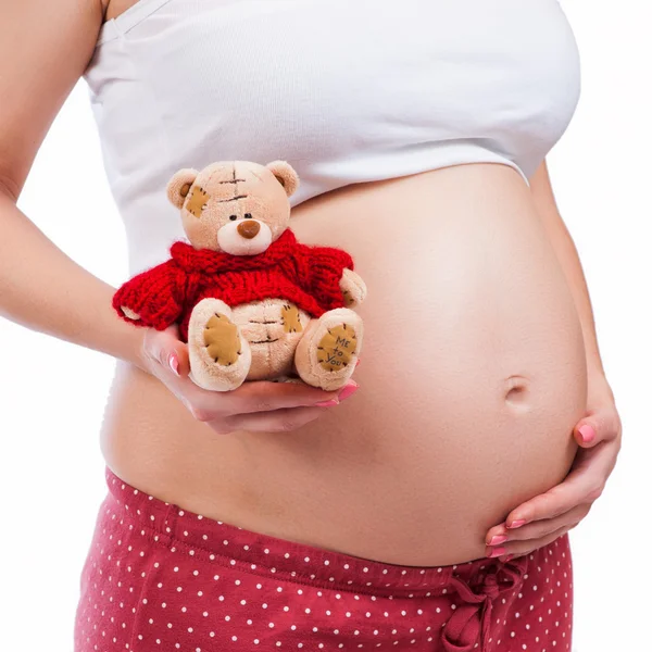 Беременная мать показывает живот и держит плюшевого мишку. — стоковое фото