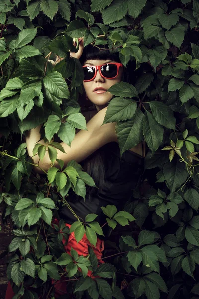 Girl wearing red sun glasses over foliage background — Stock Photo, Image