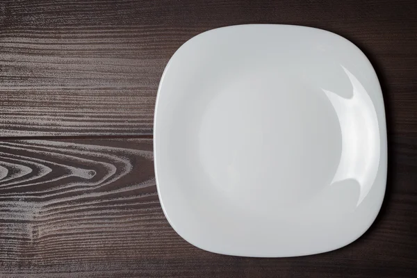 Белая квадратная тарелка на деревянном коричневом столе — стоковое фото