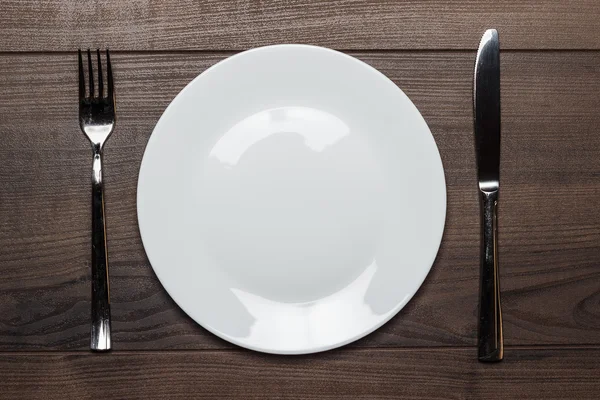 Bílá deska s nožem a vidličkou na dřevěný stůl — Stock fotografie