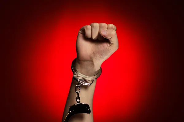 Fist and handcuffs opened over red background