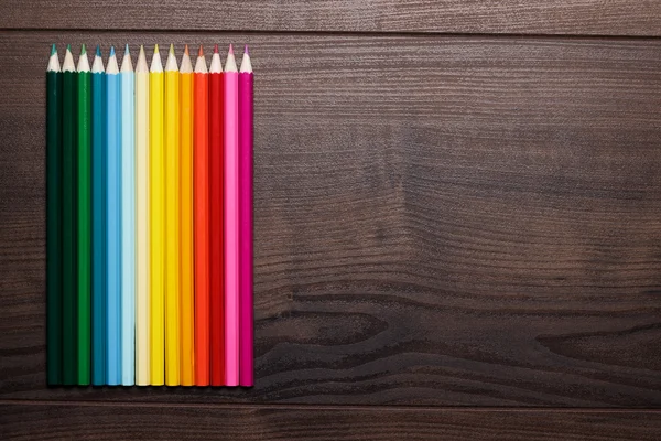 Barevné tužky nad hnědý dřevěný stůl pozadí — Stock fotografie