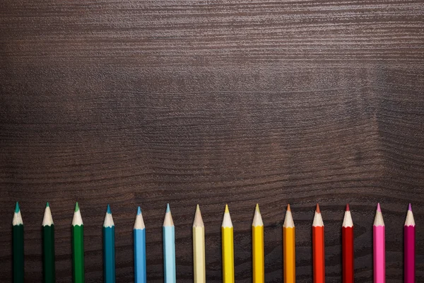 Mångfärgade pennor över bruna träbord bakgrund — Stockfoto