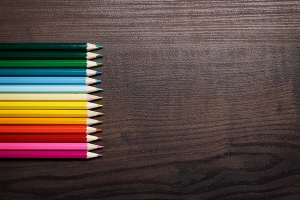 Veelkleurige potloden over bruin tabelachtergrond — Stockfoto