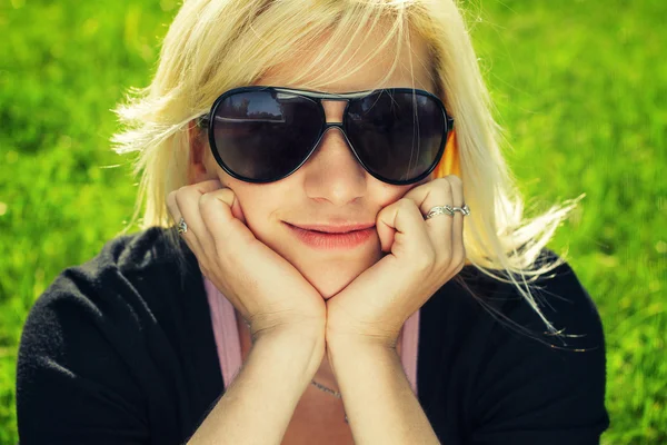 Νεαρό κορίτσι σε γυαλιά ηλίου που κάθεται στο γρασίδι — Φωτογραφία Αρχείου