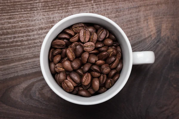 Xícara de grãos de café no fundo de madeira marrom — Fotografia de Stock