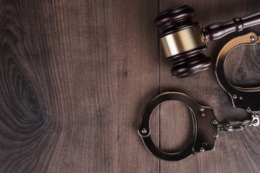Handcuffs and judge gavel on wooden background clipart