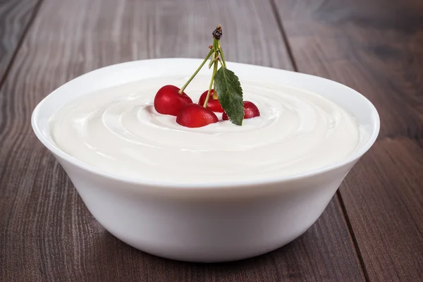 Cuenco blanco lleno de crema agria con algunas cerezas — Foto de Stock