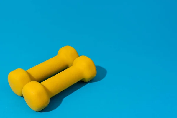 Photo of yellow fitness dumbbells over blue backgound with copy space — Stock Photo, Image