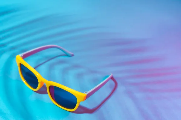 Крупним планом зображення сонцезахисних окулярів на бірюзовому синьому фоні з тіні пальми — стокове фото