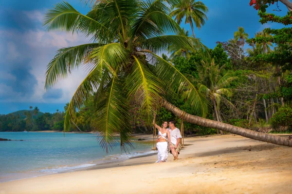 Verliebtes Paar auf einer Schaukel unter einer Palme am Strand — Stockfoto