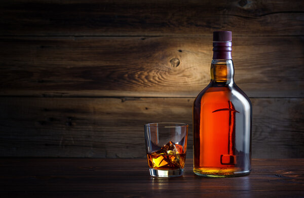 бутылка и стакан виски со льдом на деревянном фоне

