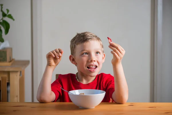 Χαριτωμένο αγόρι παίζει με granola στο πρωινό. Αυθεντικές εκφράσεις. — Φωτογραφία Αρχείου