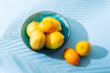 Mavi arka planda parlak sarı limonlu bir kase. Güneşli bir sabah, sert bir ışık, gölgeler.