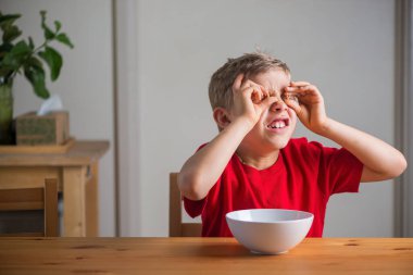 Kahvaltıda tahıl gevreğiyle oynayan tatlı çocuk. Yaşam tarzı portresi. Doğal ışık. Özgün ifadeler.