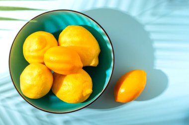 Mavi arka planda parlak sarı limonlu bir kase. Güneşli bir sabah, sert ışık, gölgeler. Seçici odak noktası.
