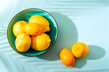 Mavi arka planda parlak sarı limonlu bir kase. Güneşli bir sabah, sert ışık, gölgeler. Seçici odak noktası.