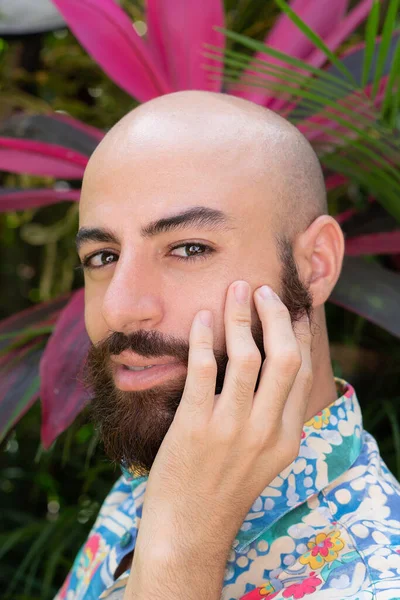 Bearded man in a blue shirt with prints touching his face — Stockfoto